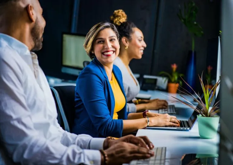 Mehrere Personen sitzen an einem Schreibtisch und arbeiten an Laptops in einem modernen Büro – symbolisiert Upskilling, Weiterbildung und digitale Zusammenarbeit.