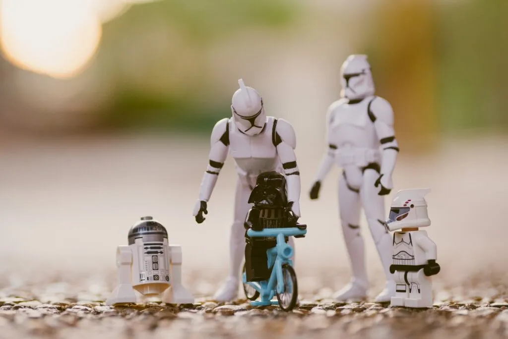 Vier Lego-Figuren im Star-Wars-Stil stehen auf einer rauen Oberfläche, eine Figur sitzt auf einem blauen Fahrrad, umgeben von weiteren Charakteren.