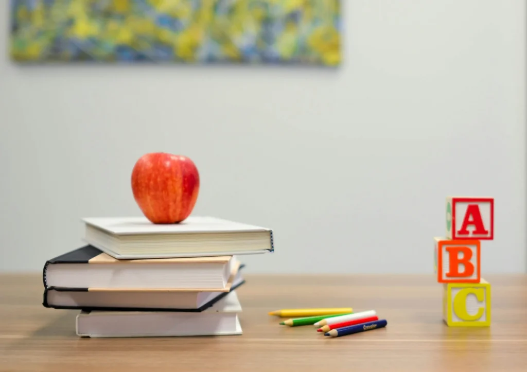 Gestapelte Bücher mit rotem Apfel, bunte Buntstifte und ABC-Bauklötze auf einem Tisch – Symbol für Lernen und Bildung