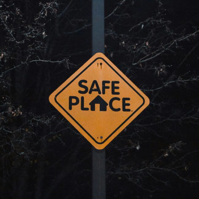 in gelbes Verkehrsschild mit der Aufschrift „SAFE PLACE“ vor dunklem Hintergrund.
