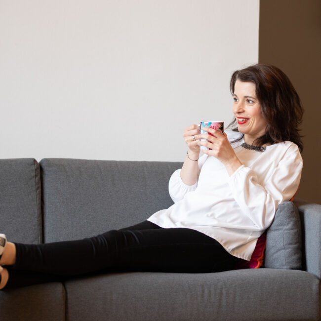 Person sitzt entspannt auf einem grauen Sofa und hält ein Smartphone in der Hand – Moment der Ruhe während eines Events