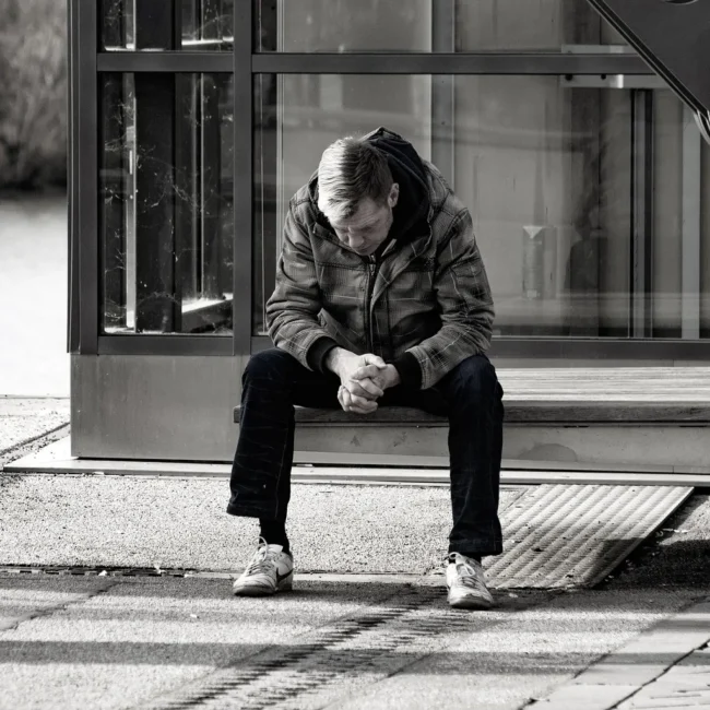 Person sitzt allein auf einer Bank in einer urbanen Umgebung – Symbol für Isolation und die Bedeutung von Prävention