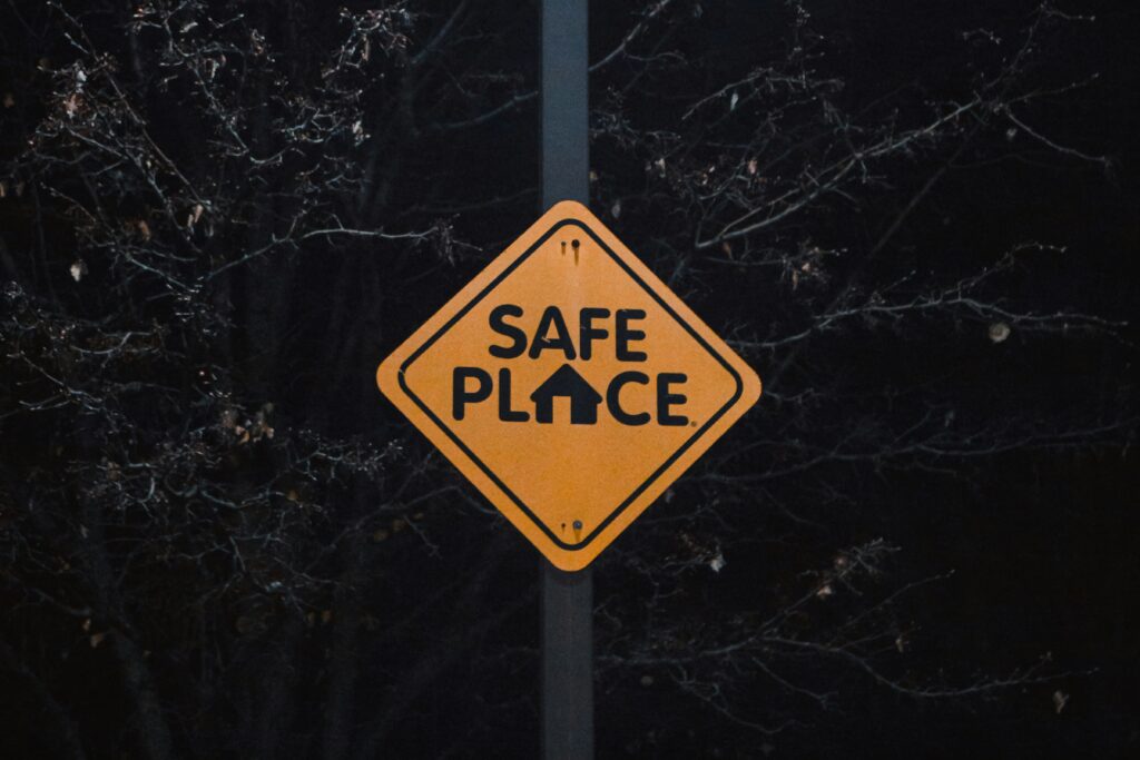 in gelbes Verkehrsschild mit der Aufschrift „SAFE PLACE“ vor dunklem Hintergrund.