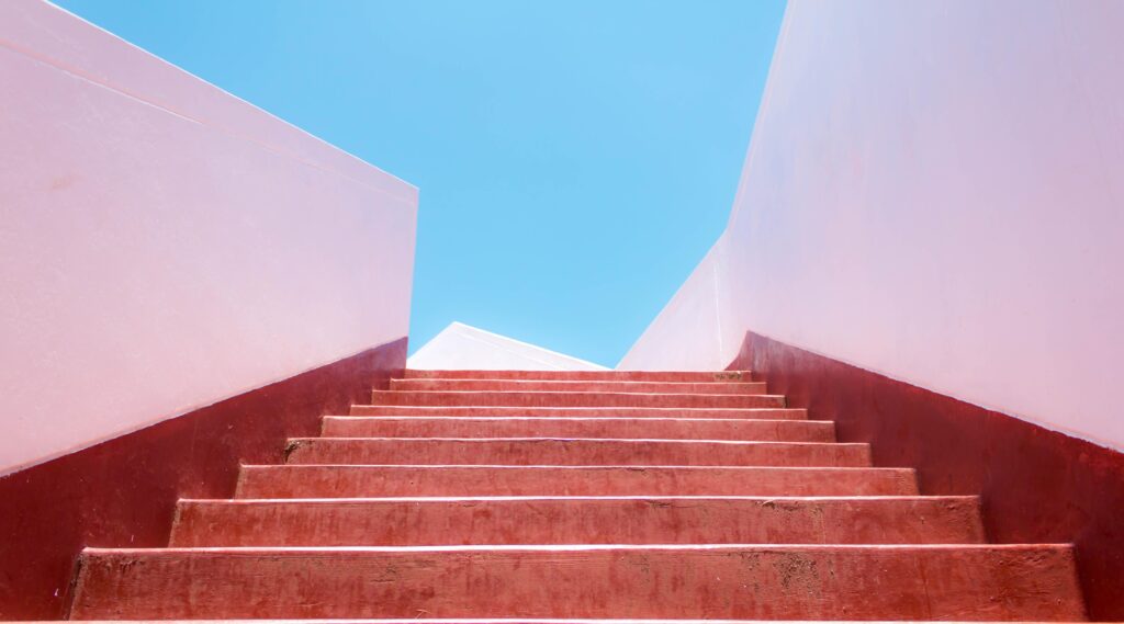 Rote Treppe führt nach oben zu blauem Himmel als Symbol für persönliche Entwicklung und Zukunft der Arbeit