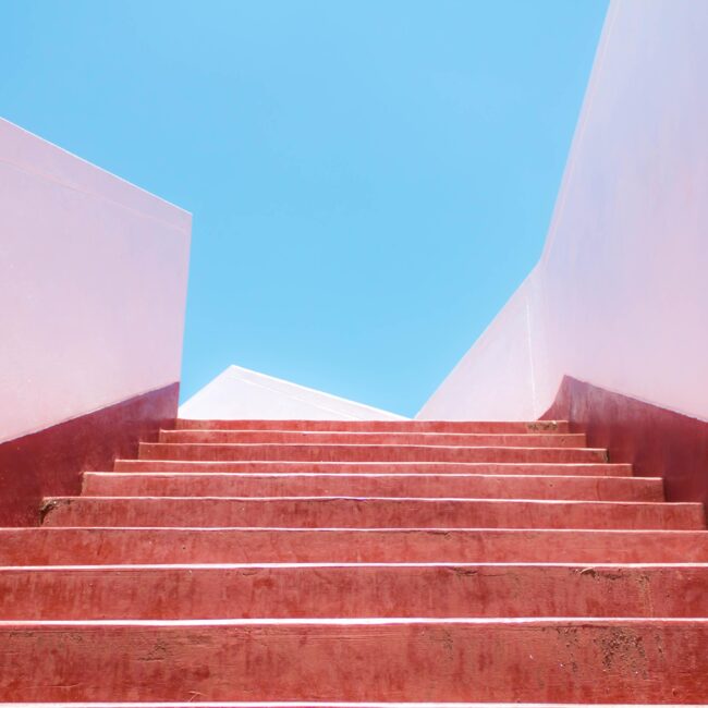 Rote Treppe führt nach oben zu blauem Himmel als Symbol für persönliche Entwicklung und Zukunft der Arbeit